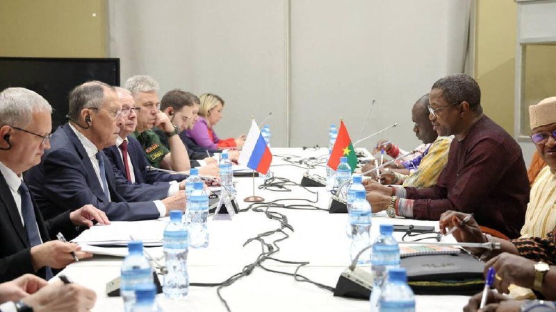 Delegations sit on opposite sides of a conference table with microphones, water bottles, and small Russian and Burkina Faso flags placed between them.