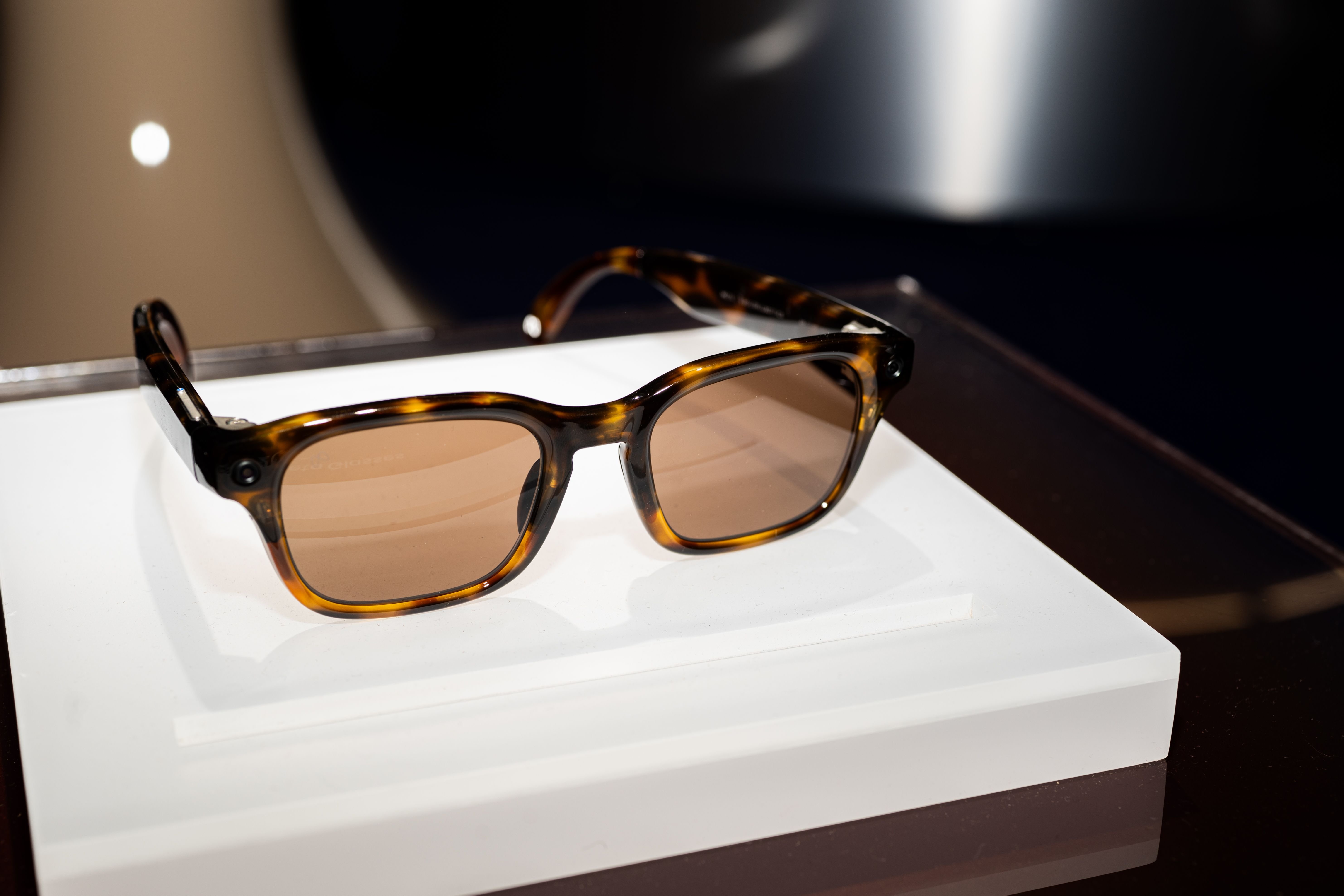 Tortoiseshell-framed sunglasses with tinted lenses rest on a white rectangular display block against a dark background.