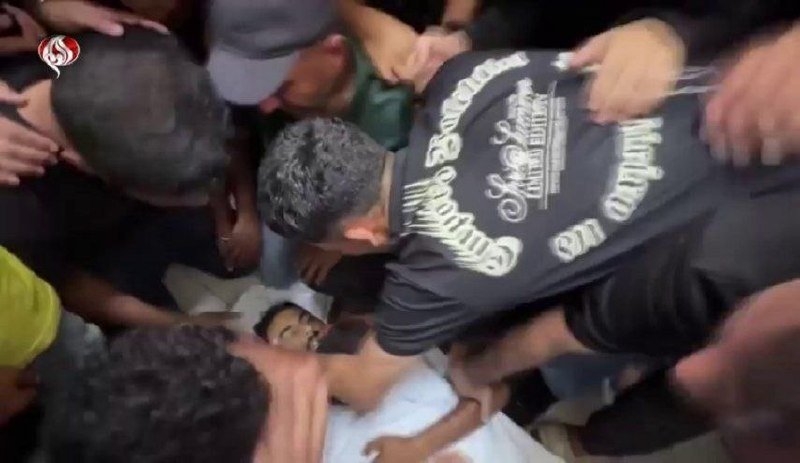 A crowd of people surrounds and tends to an injured person lying on the ground in a chaotic scene.