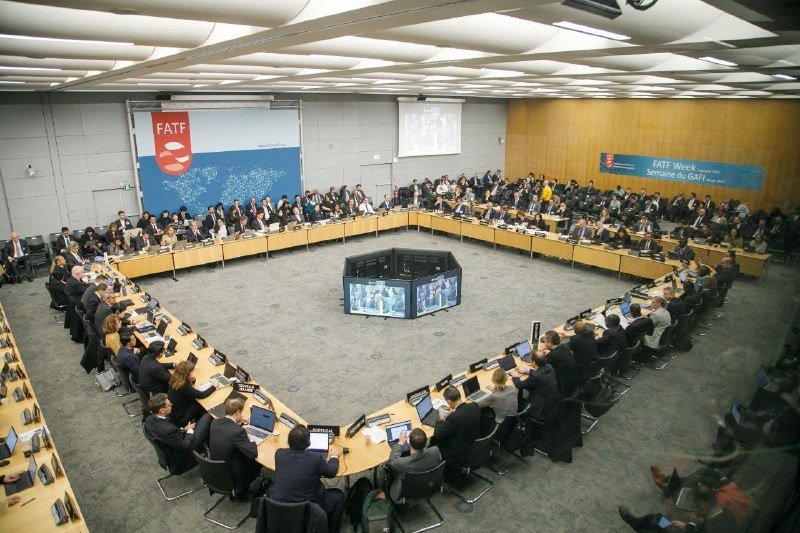 Attendees sit around a large octagonal conference table with laptops, beneath a "FATF" logo banner and a "FATF Week Semaine du GAFI" sign on the wall.