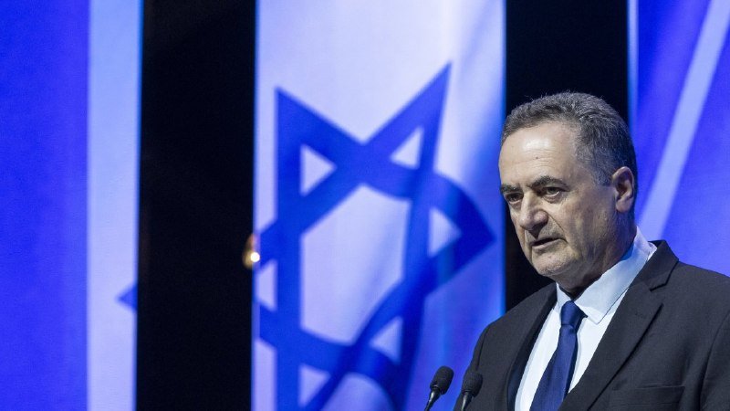A gray-haired man in a dark suit and blue tie stands at microphones with Israeli flags displayed behind him.