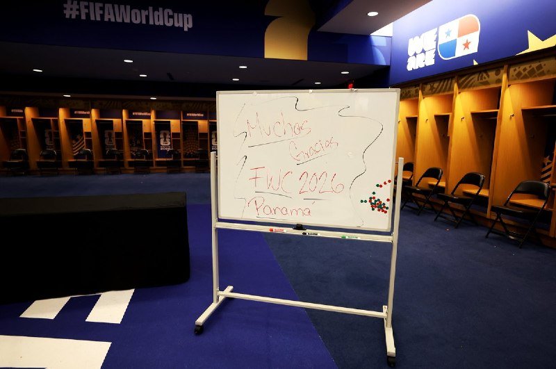A whiteboard displaying handwritten Spanish text reading "Muchas Gracias, FWC 2026, Panama" stands in a locker room beneath a "#FIFAWorldCup" banner and empty player stalls.