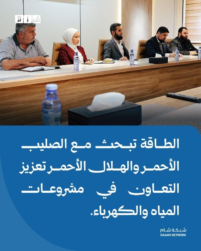 Five people sit at a long conference table with water bottles and notebooks, with Arabic text on a blue panel below reading "Shaam Network."