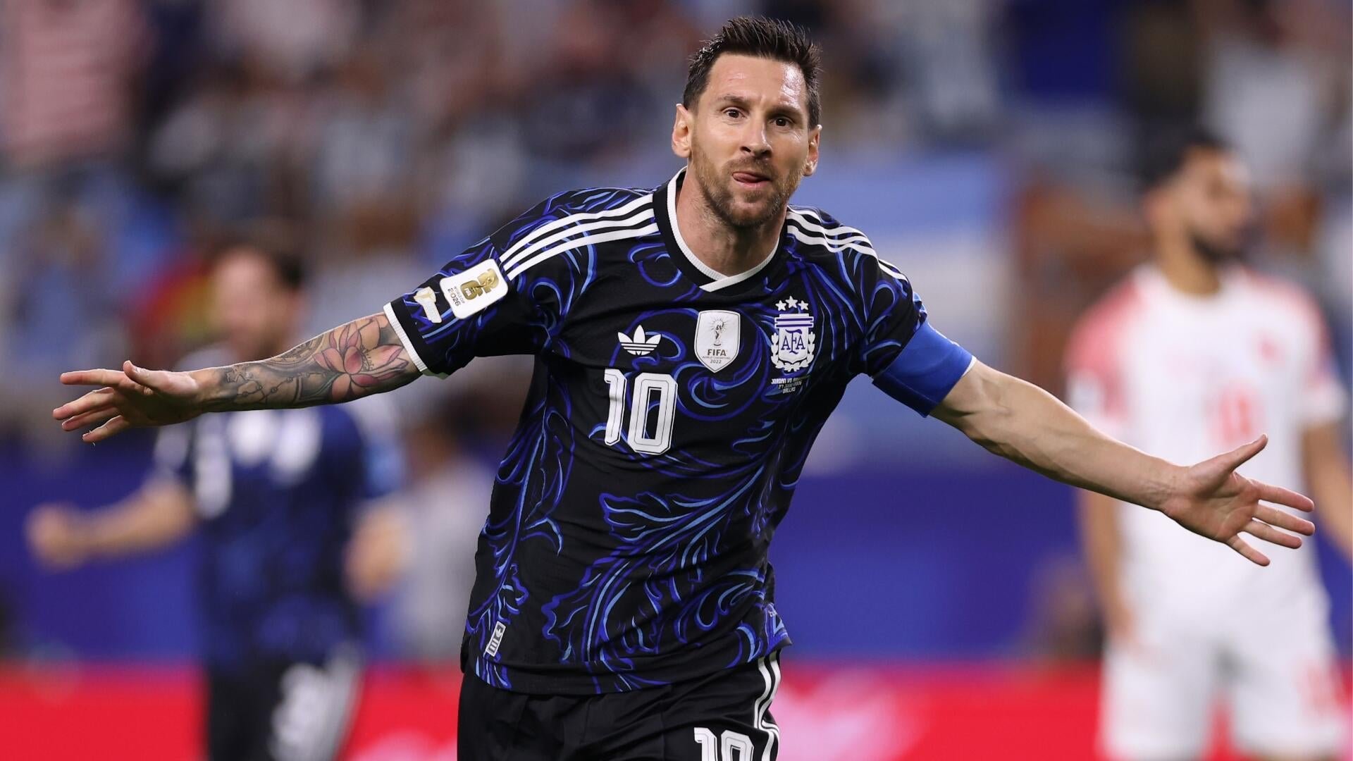 A bearded soccer player in a black and blue number 10 jersey with arms outstretched celebrates on the field during a match.