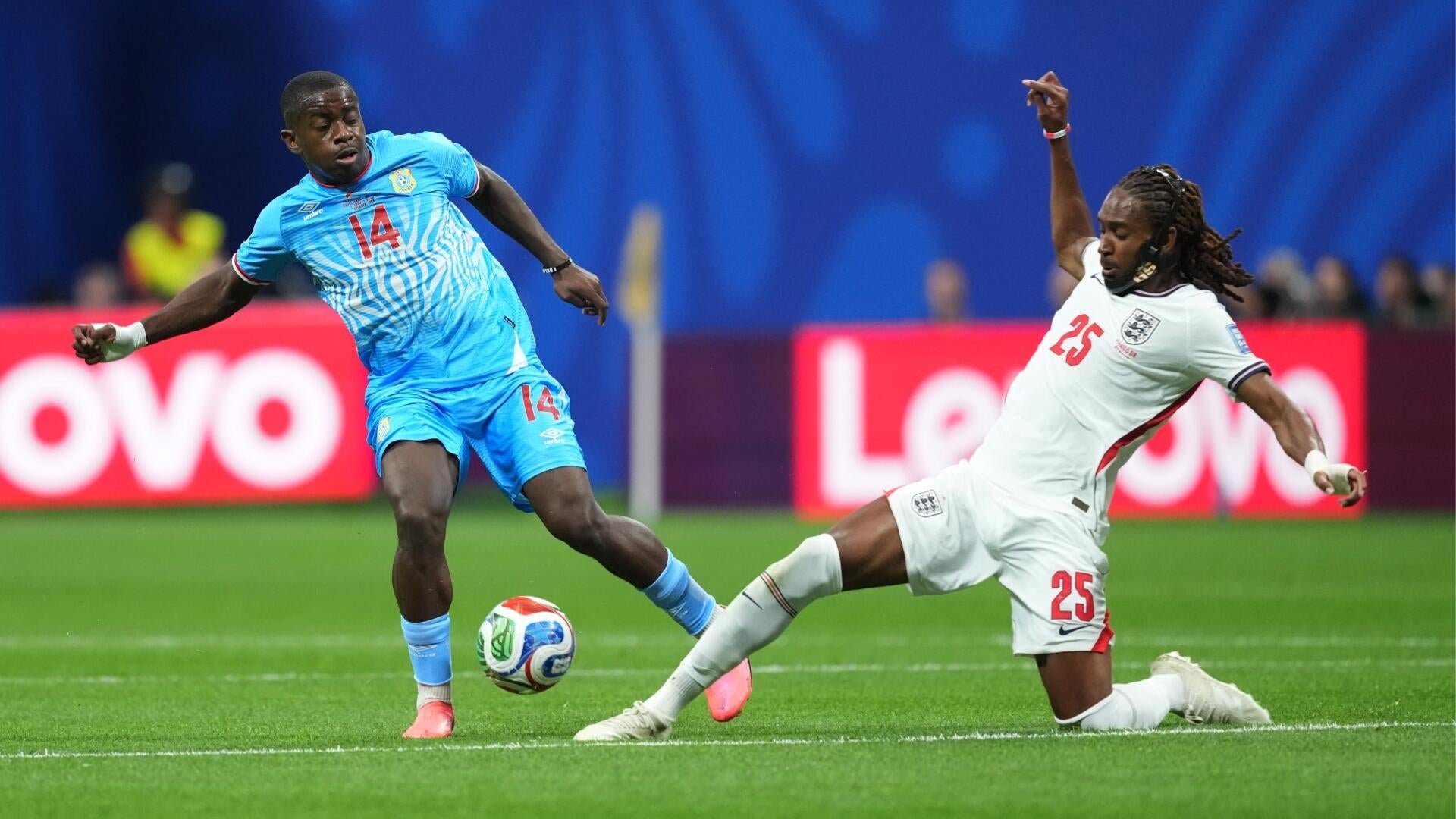Two soccer players, one in a light blue #14 kit and another in a white #25 kit, compete for the ball on a green field during a match.