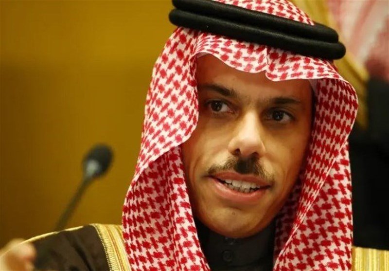 A man wearing a red-and-white checkered keffiyeh and black agal speaks at a microphone during what appears to be a formal indoor setting.