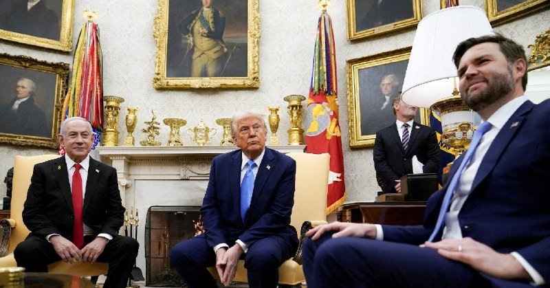 Three men in suits sit and stand in an ornate room featuring a fireplace, gilded vases, framed portraits, and ceremonial flags.