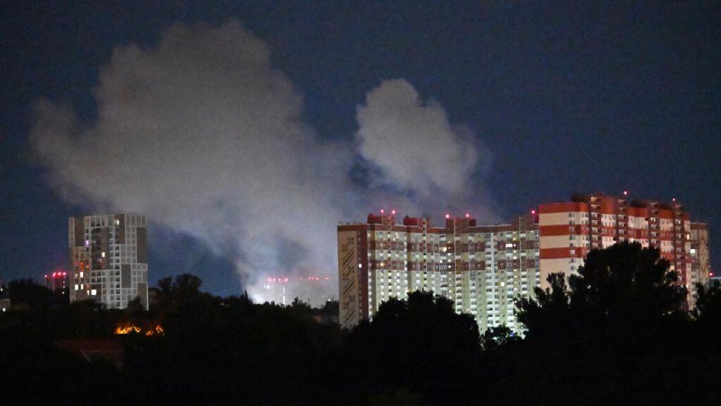 Illuminated high-rise buildings stand at night beneath a sky filled with large clouds.