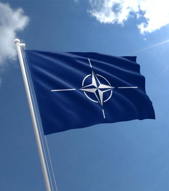 A dark blue flag bearing a white compass-star emblem waves from a flagpole against a partly cloudy blue sky.