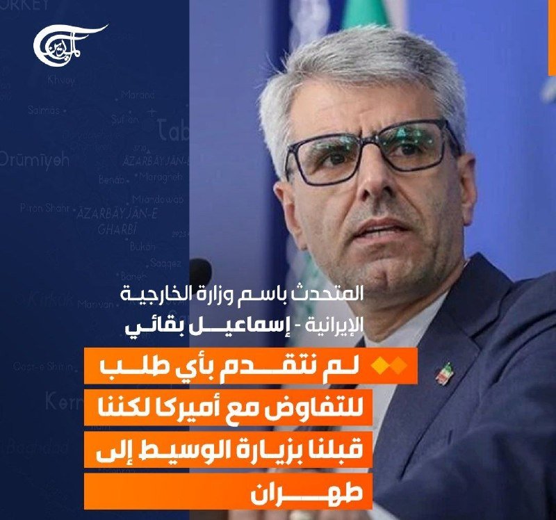 A gray-haired man in glasses and a suit speaks at a microphone, with Arabic text and a logo overlaid on the image.