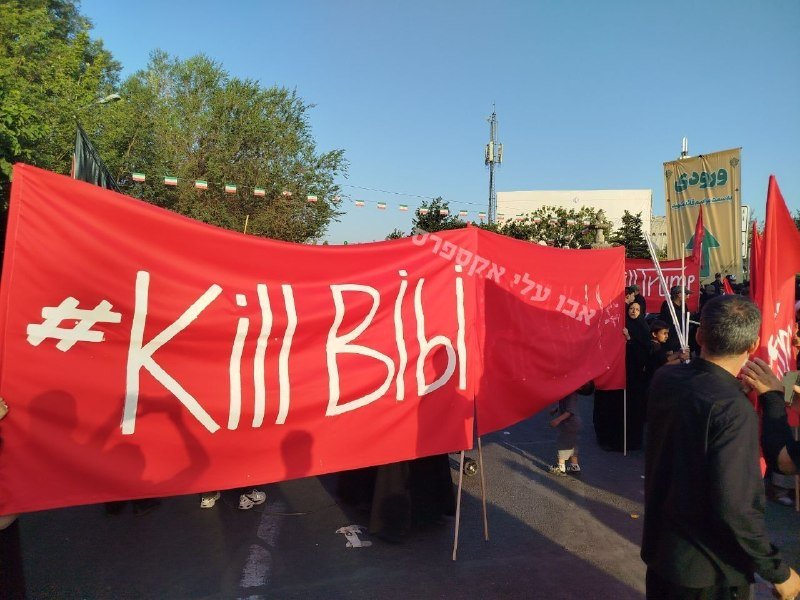A crowd carries a large red banner reading "#KillBill" alongside smaller red flags and a tan banner with Arabic/Persian script during an outdoor daytime gathering.