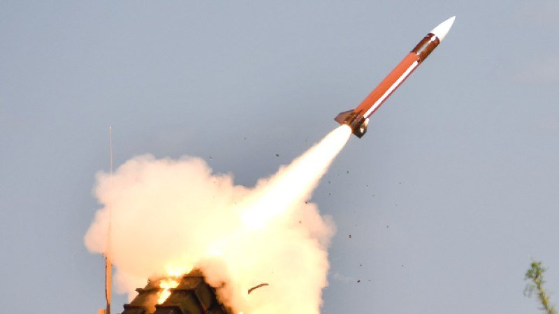 A missile launches into a hazy sky, propelled by a large burst of flame and thick smoke from a launcher visible at the bottom.