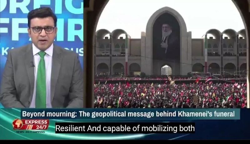 A news anchor in a suit and green tie presents a split-screen broadcast showing a massive crowd beneath a large portrait at a public gathering.