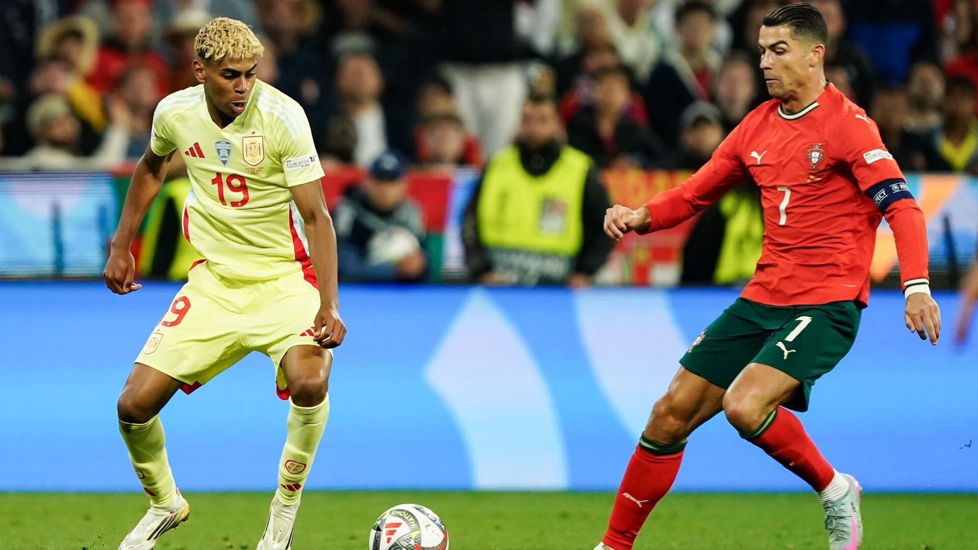 A player in a yellow Spain jersey marked number 19 dribbles a soccer ball while being challenged by an opposing player in a red jersey marked number 7.