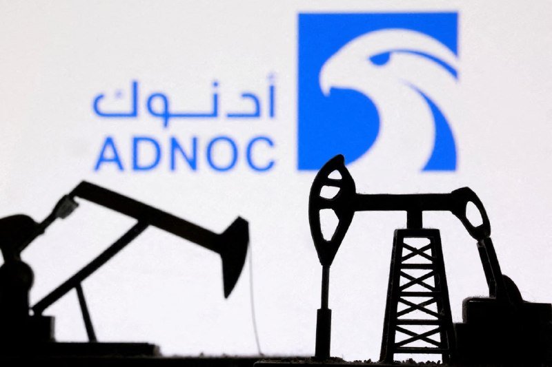 Silhouetted miniature oil pumpjacks stand in front of a projected screen displaying the blue ADNOC logo with Arabic script and a falcon emblem.