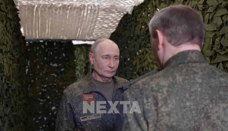A balding man in military camouflage stands facing another uniformed officer inside a tent lined with camouflage netting, beneath a "NEXTA" watermark.