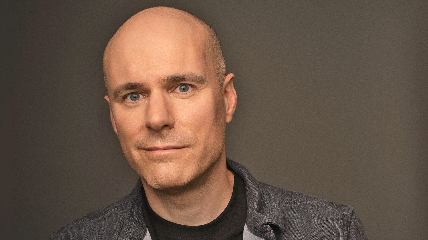 A large crowd gathers at night before an outdoor movie screening, with a giant screen displaying a woman and subtitles visible beside an illuminated ornate building.