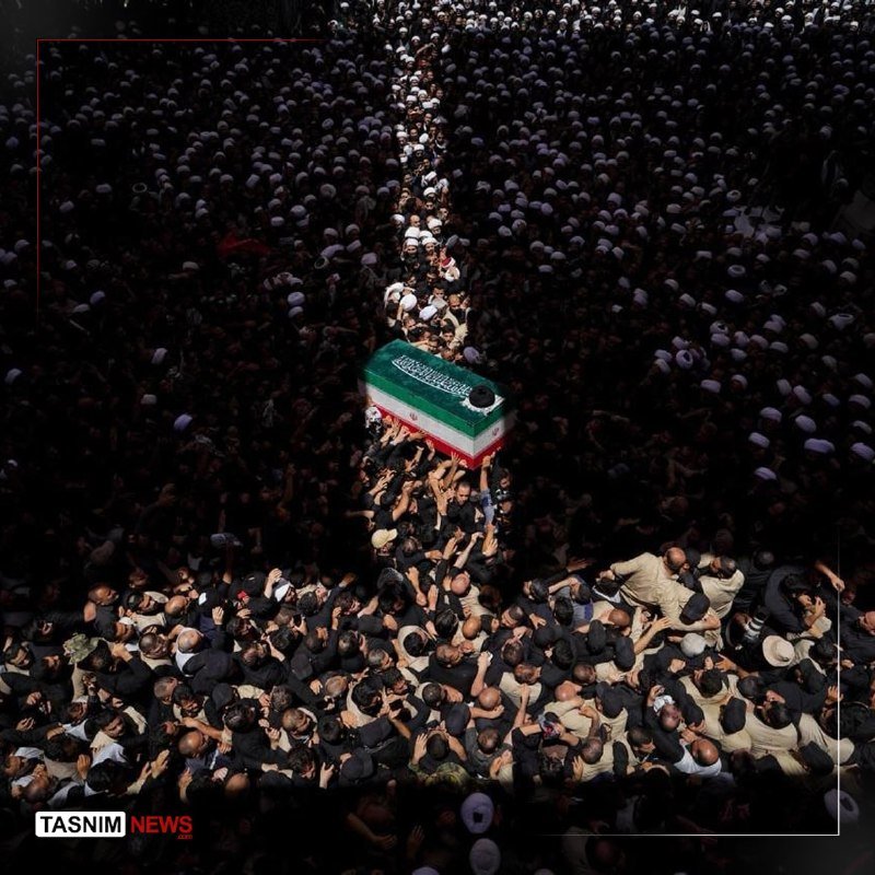 A massive crowd carries a flag-draped casket through a narrow passage, viewed from above.