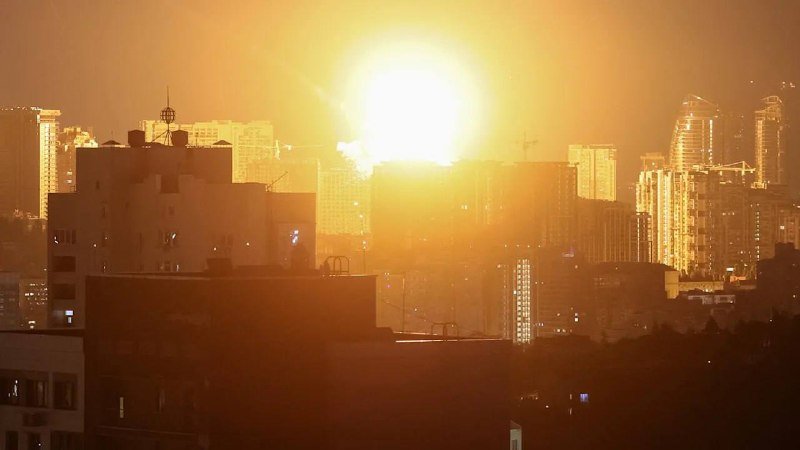 A bright orange glow illuminates a city skyline of high-rise buildings at dawn or dusk.