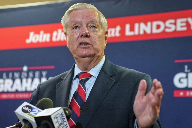 A white-haired man in a dark suit and striped tie speaks while gesturing beside ABC News microphones, with a "Lindsey Graham" campaign backdrop behind him.