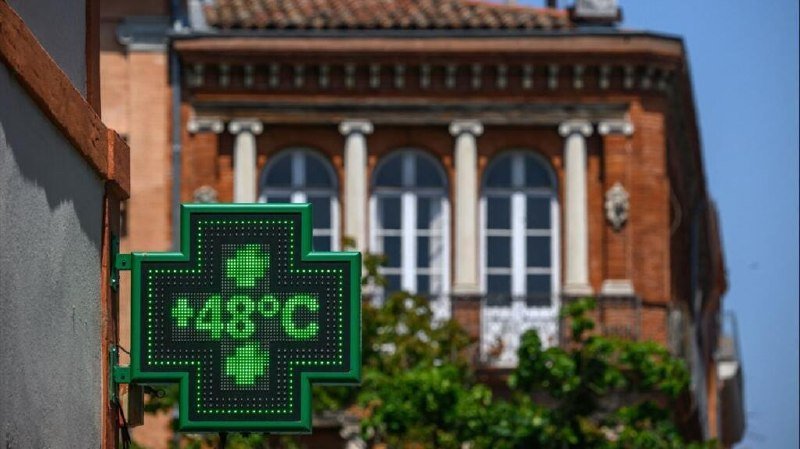 An illuminated green pharmacy cross sign displays "28°C" in front of a brick building with arched windows.