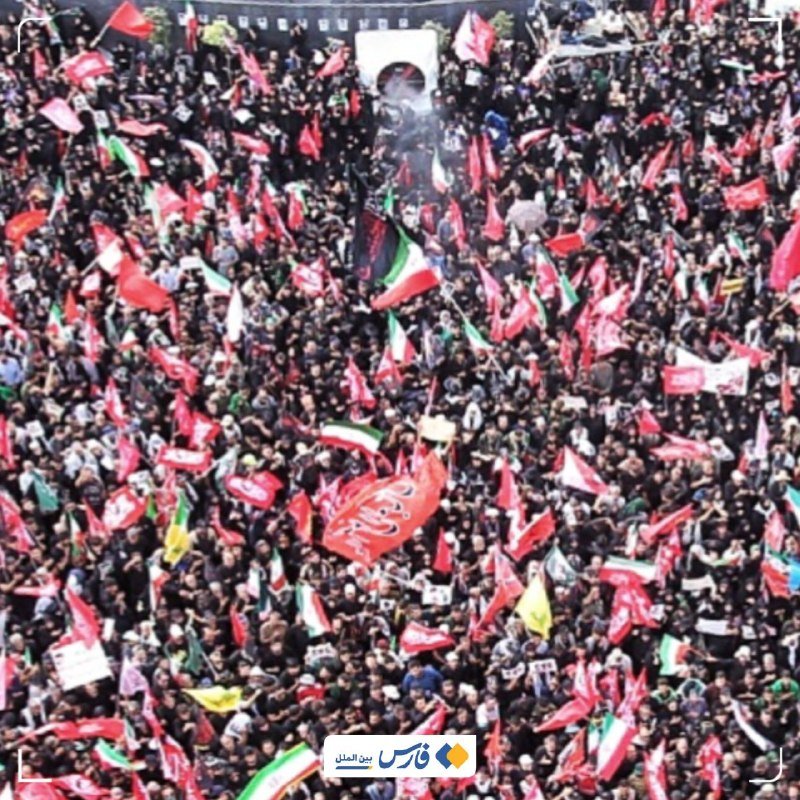 A large crowd waves numerous red flags and a banner with Arabic script, with one Iranian flag visible.