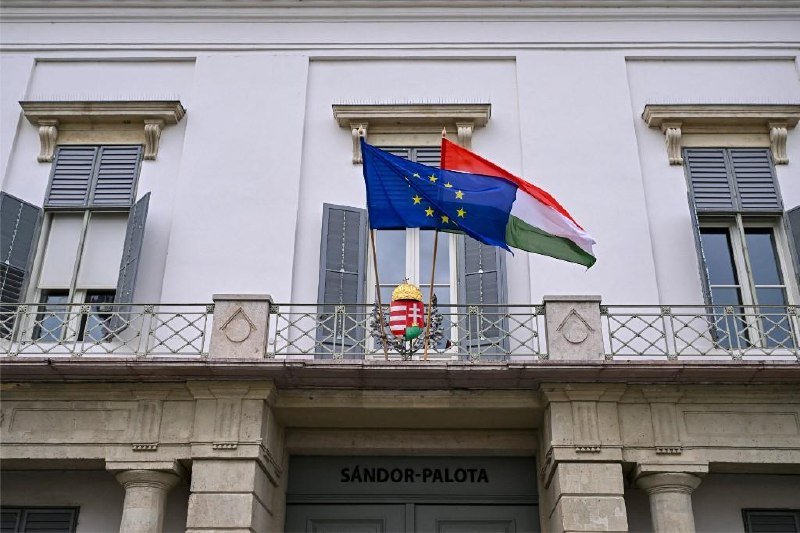 The Hungarian and European Union flags fly above a balcony displaying a coat of arms outside the building labeled "SÁNDOR-PALOTA."