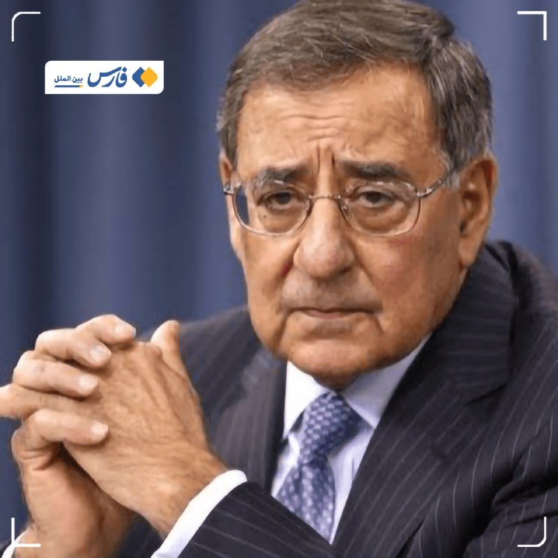 An older man in a dark pinstripe suit, white shirt, and blue patterned tie sits with clasped hands against a blue curtain backdrop, wearing rimless glasses with a serious expression.