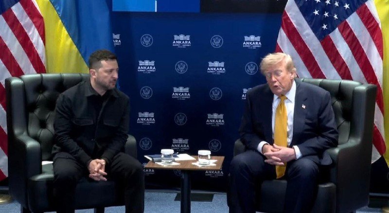 Two men sit in green leather armchairs facing forward, with a small table between them holding water glasses, against a blue backdrop displaying "ANKARA" and US and Ukrainian flags.