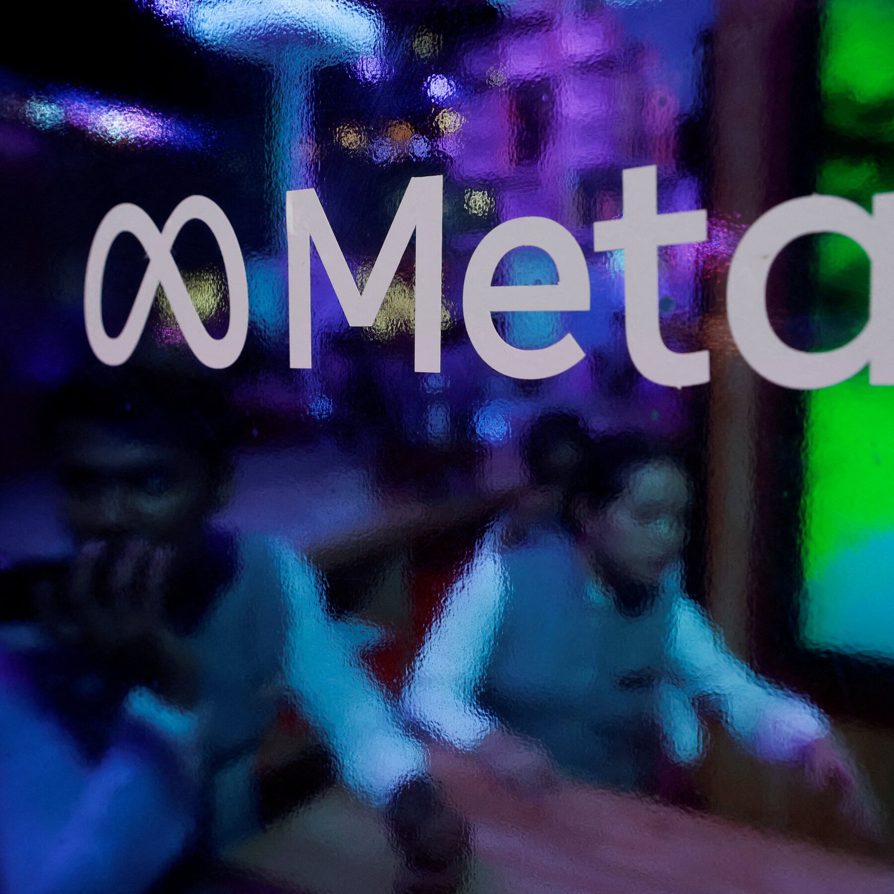 Close-up of the Meta logo in white lettering on a textured, multicolored background of blue, purple, and green hues.