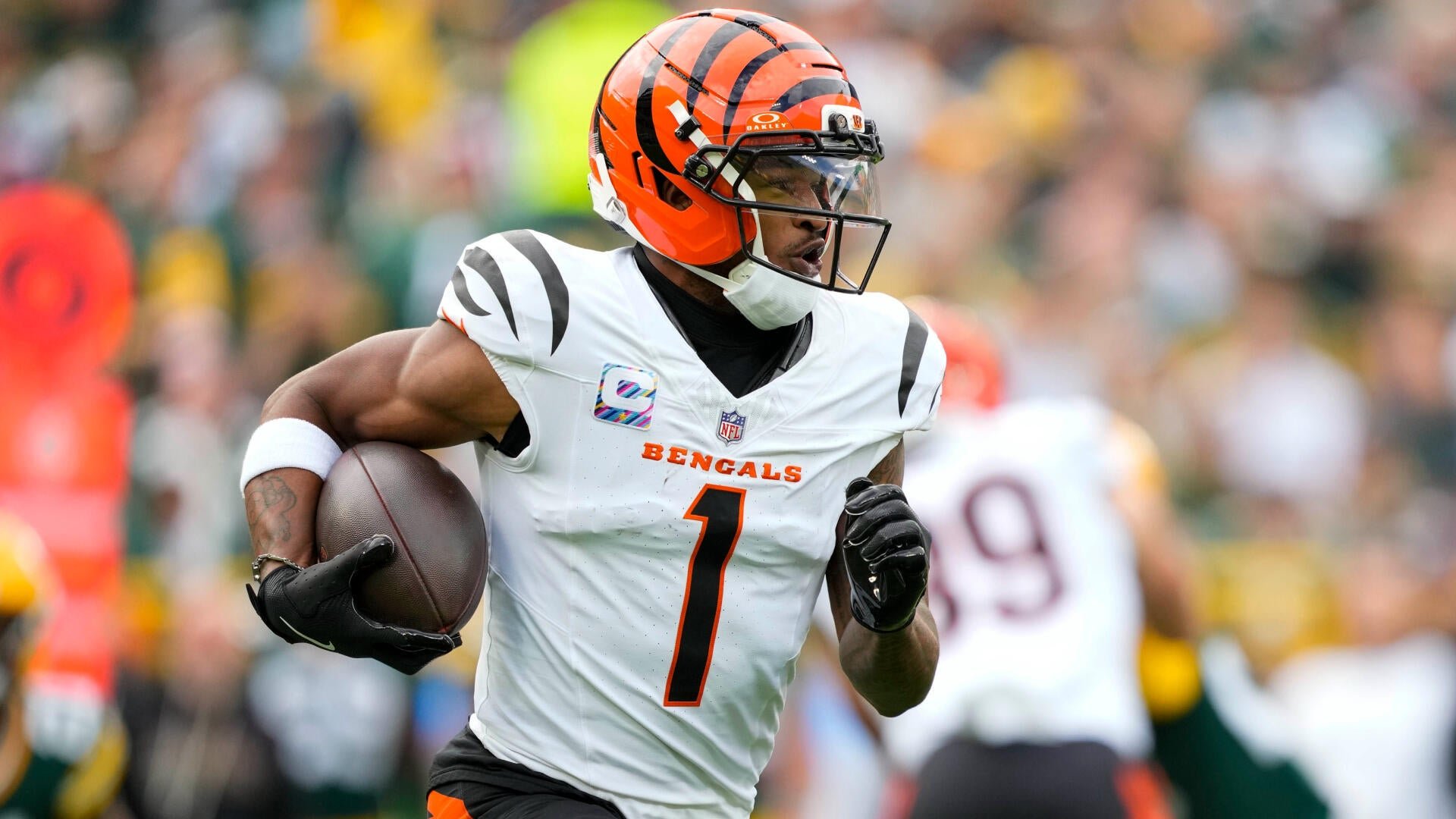 A Cincinnati Bengals player wearing jersey number 1 runs with the football tucked under his right arm during an NFL game, with blurred spectators visible in the background.