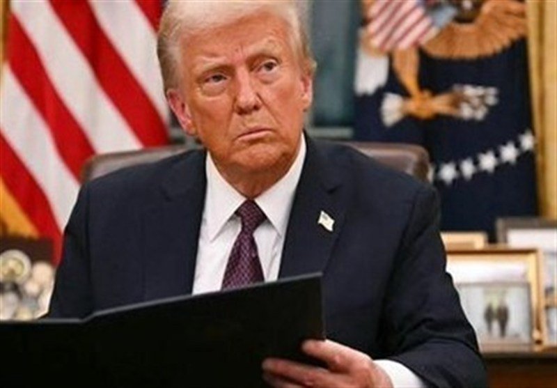 A man in a dark suit and burgundy tie reads from a black folder, seated before an American flag and presidential seal.