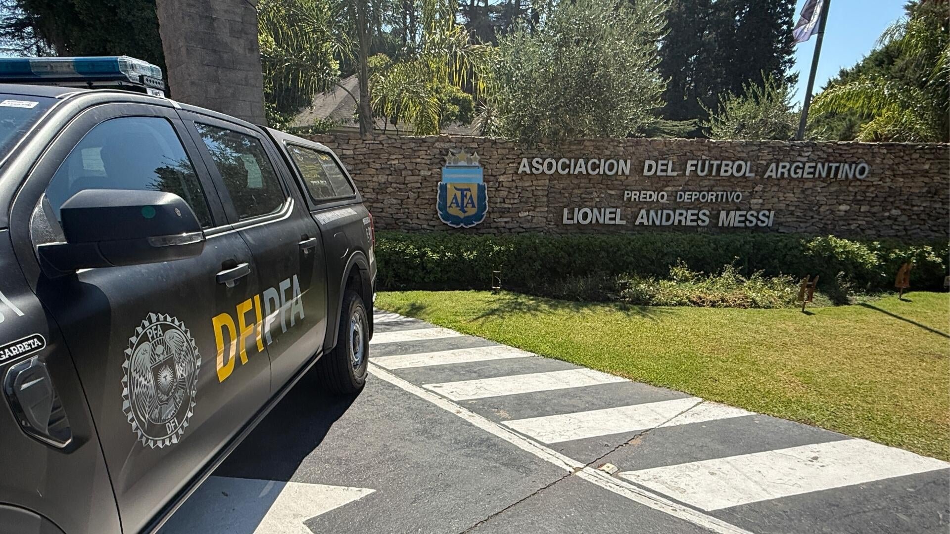 A black DFI-PFA police pickup truck is parked in front of a stone wall displaying the AFA crest and the inscription "Asociación del Fútbol Argentino, Predio Deportivo Lionel Andrés Messi."