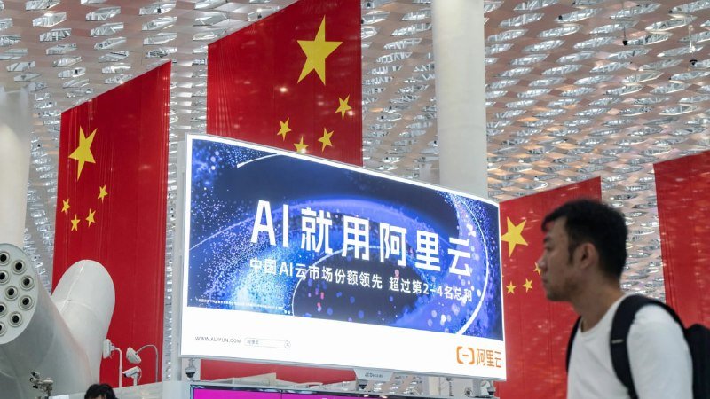 A man walks past a large billboard displaying Chinese text and "AI" branding, set against Chinese national flags and a modern lattice ceiling.