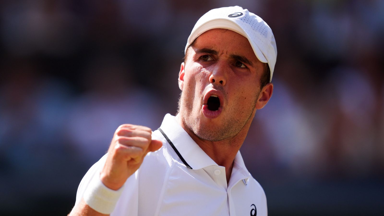 A tennis player in white lies on his back on a grass court with legs raised, as a crowd of spectators watches and applauds behind him; a purple floral graphic reads "HIGHLIGHTS."