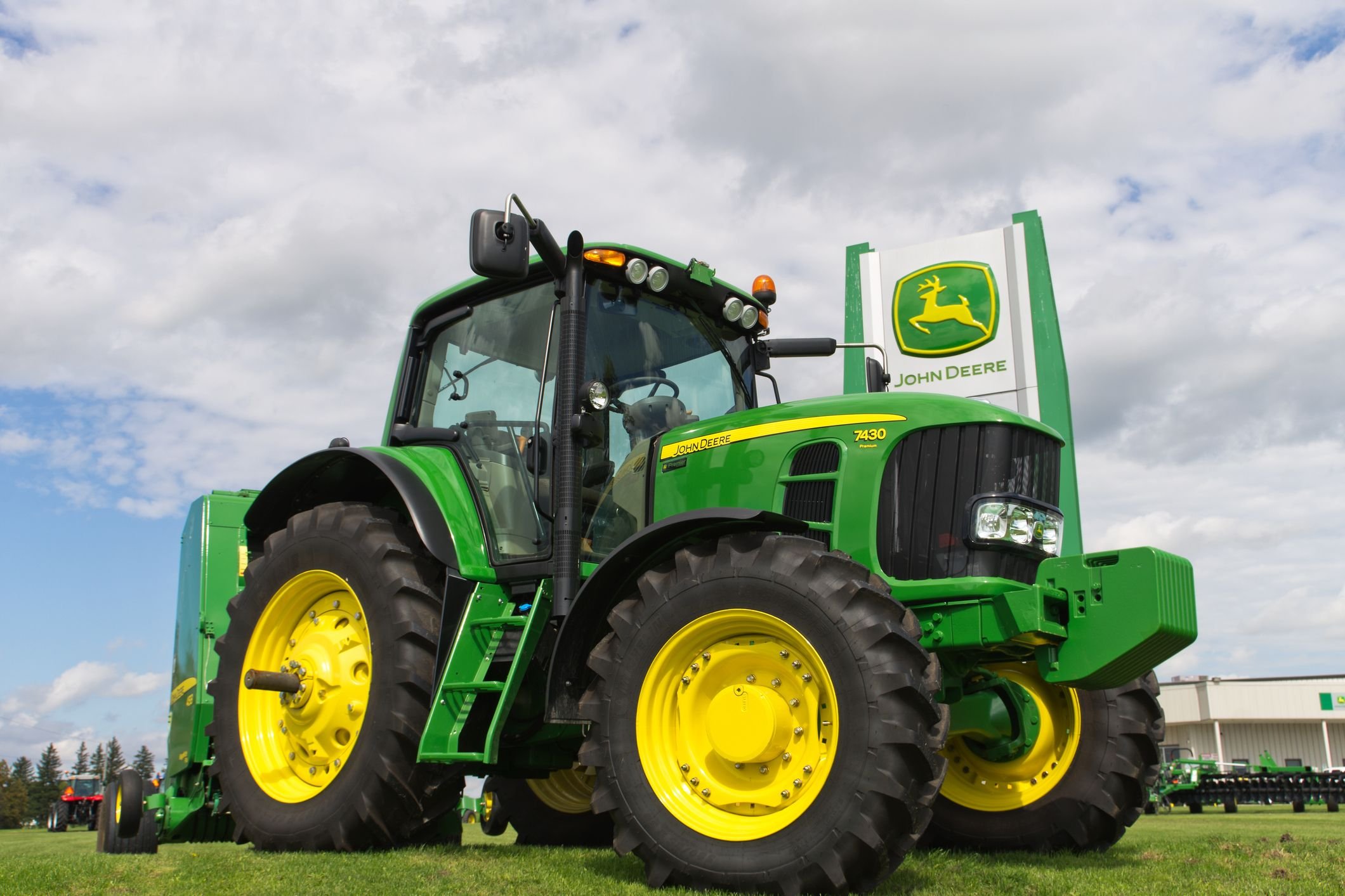 A green and yellow John Deere 7430 tractor with large yellow-wheeled tires sits on grass under a cloudy sky.