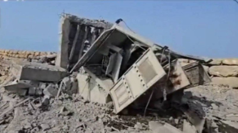 Collapsed concrete structure with exposed rebar and debris scattered on the ground under a clear blue sky.