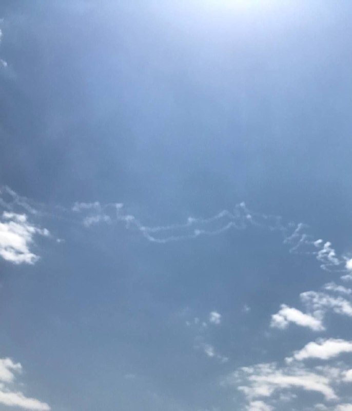 Bright sun shines through scattered wispy clouds in a blue sky.