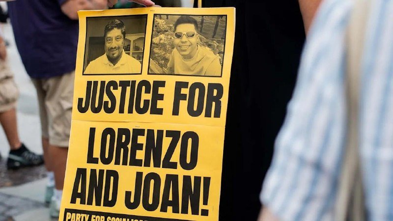 A yellow protest sign displaying two black-and-white portraits reads "JUSTICE FOR LORENZO AND JOAN!" as pedestrians walk by on a street.