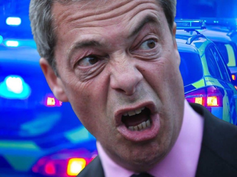 A man in a dark suit and pink shirt shouts with an open mouth, photographed in front of blurred blue police vehicle lights.