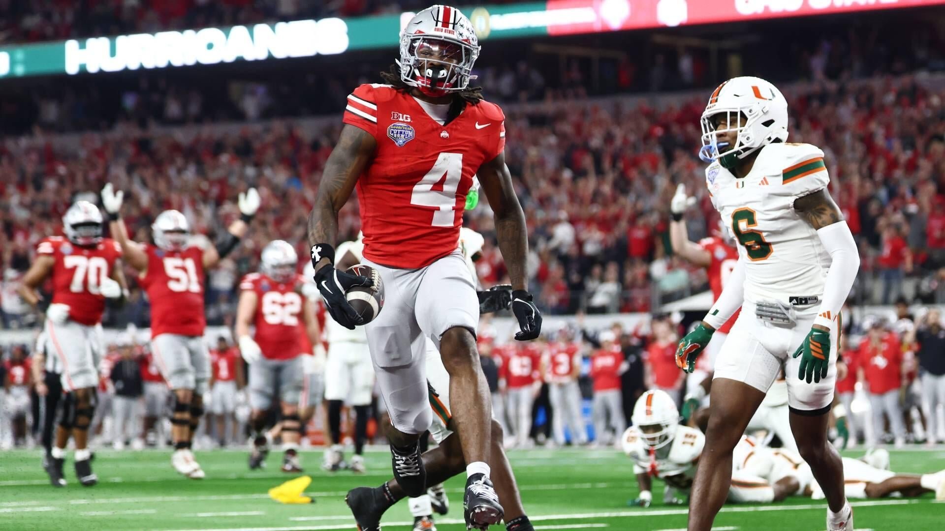 A football player wearing a red #4 Ohio State jersey walks across the field holding a football, while a Miami player in a white #6 jersey looks on, with teammates visible in the background.