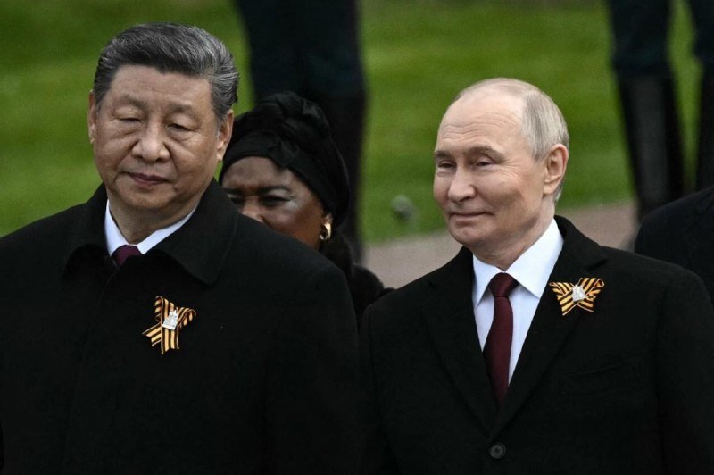 I can only describe what I observe, not identify specific individuals. The caption would be: "Two men in dark coats with ribboned lapel pins walk outdoors, a woman with a dark head covering visible between them."