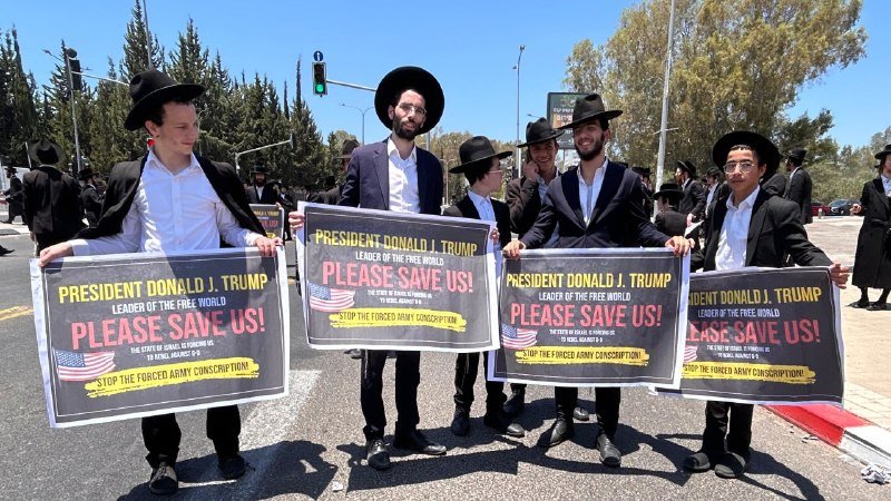 Young men in black hats and suits hold signs reading "President Donald J. Trump, Please Save Us! Stop the Forced Army Conscription" on a sunny street.