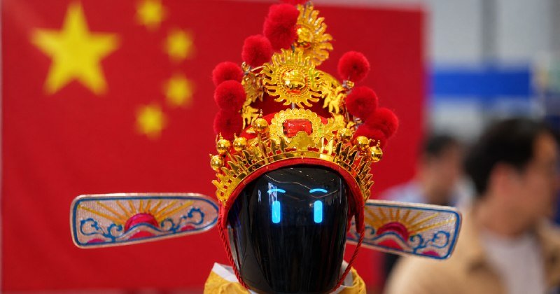 A figure wears an ornate golden headdress with red pom-poms and wing-like decorations, standing before a red Chinese flag with yellow stars.