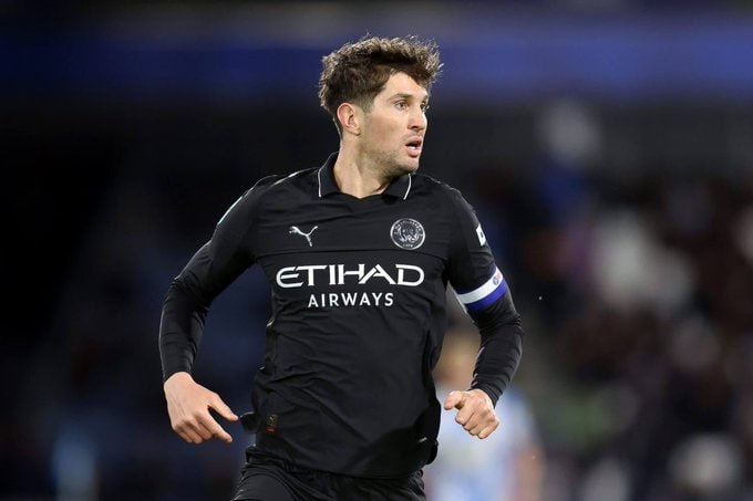 A soccer player in a black Manchester City jersey with "Etihad Airways" sponsorship and a captain's armband runs during a match.