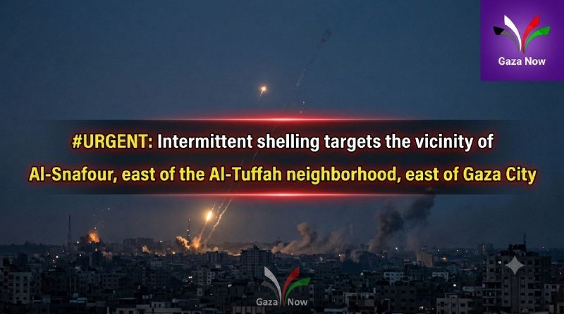 A nighttime cityscape shows plumes of smoke and bright flashes rising from a densely built urban area, with overlaid text reporting urgent shelling near Al-Sanafour.