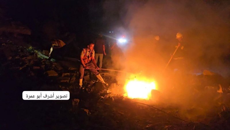Men tend a large fire amid rubble and thick smoke at night, with Arabic text reading "Photo: AFP archive" in the corner.