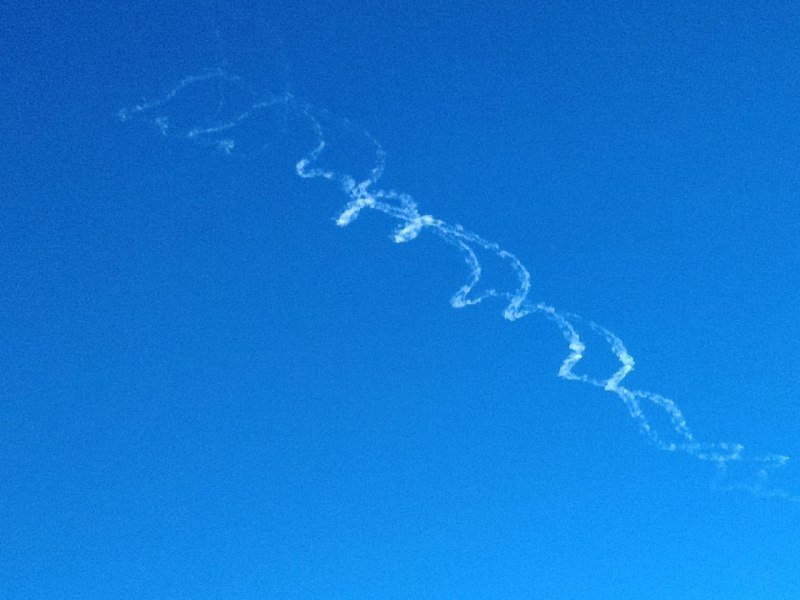A thin, wispy white contrail stretches diagonally across a clear blue sky.