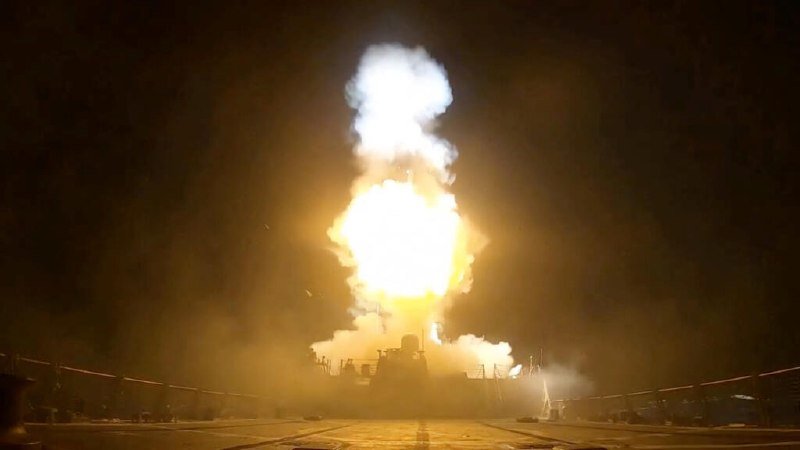 A missile launches vertically at night, producing a massive bright fireball and billowing smoke plume rising above a silhouetted naval vessel's deck.