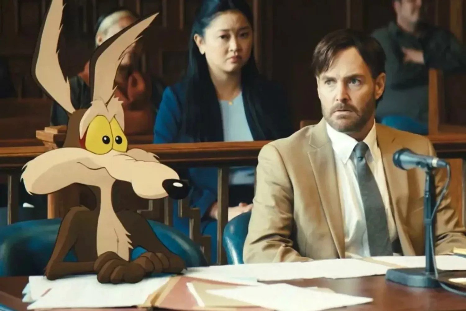 A cartoon dog sits beside a man in a tan suit at a witness table with a microphone, while onlookers watch from behind a wooden railing in a courtroom setting.